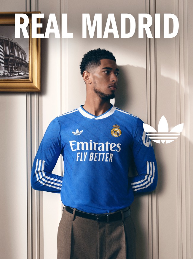 The image shows a young man wearing a blue Real Madrid soccer jersey standing in front of a framed artwork on the wall.