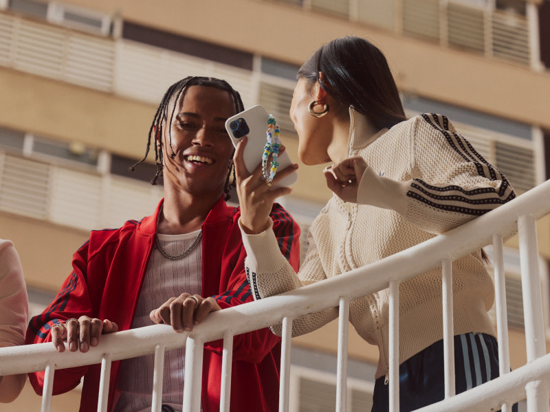 Two people leaning on a railing, looking at their phone and smiling. 