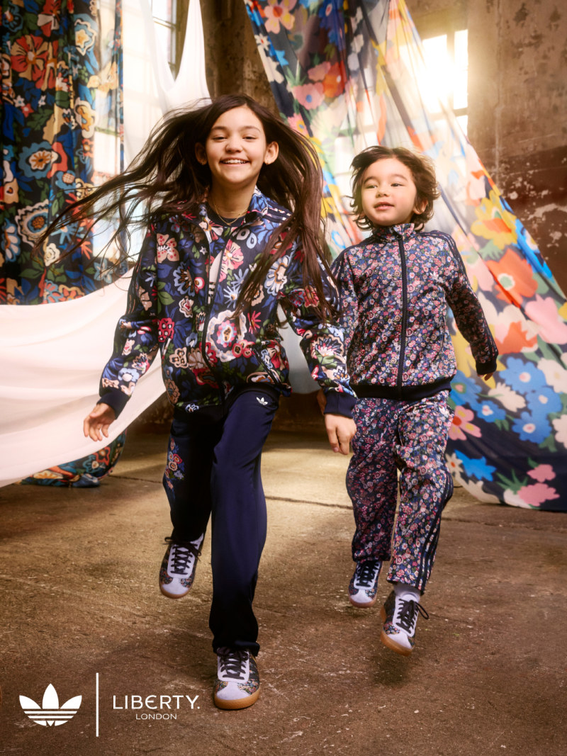 A girl and boy model the adidas Originals x Liberty London collection in an industrial space decorated with flowing, patterned fabric.