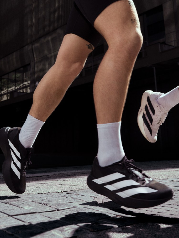 Close-up running shot of black Adizero EVO SL with white stripes and white EVO SL in the background.