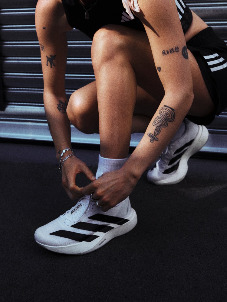 Close-up image of a woman bending to tie the shoelaces on white Adizero EVO SL with black stripes.
