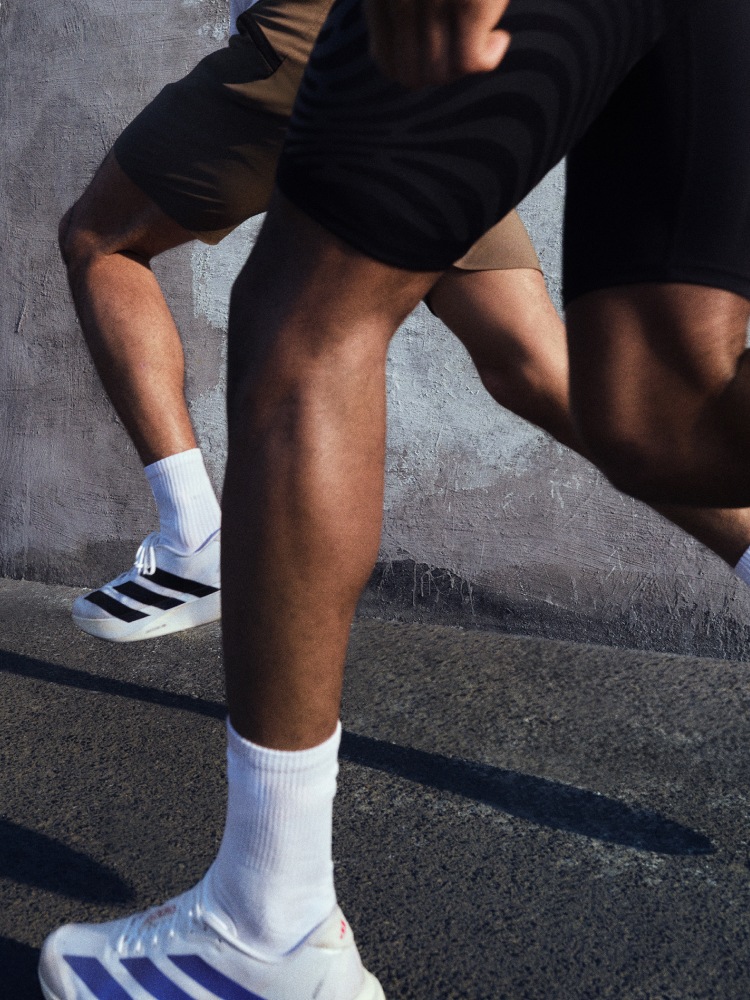 Running close-up image, featuring two white Adizero EVO SLs: one with black stripes, one with blue.