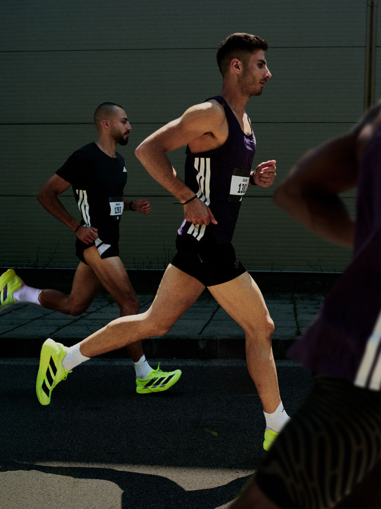 Two male athletes in athletic gear are running on a track, with a dark background behind them.