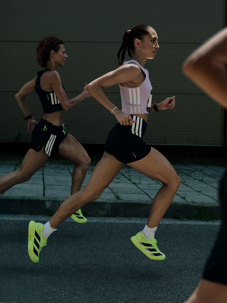 Two female athletes in athletic gear are running on a track, with a dark background behind them.