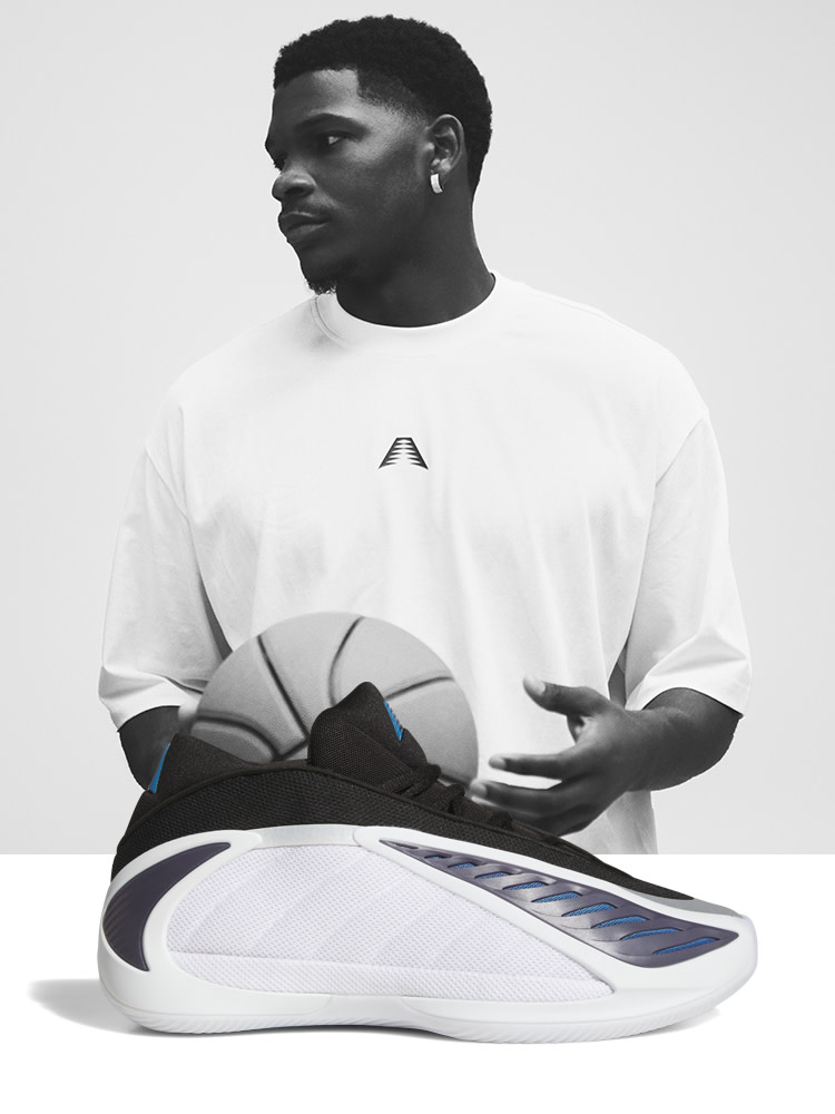 The image depicts a young man wearing a white t-shirt and holding a pair of futuristic-looking sneakers in his hands. The background is a plain, light-colored surface, creating a minimalist and focused composition.