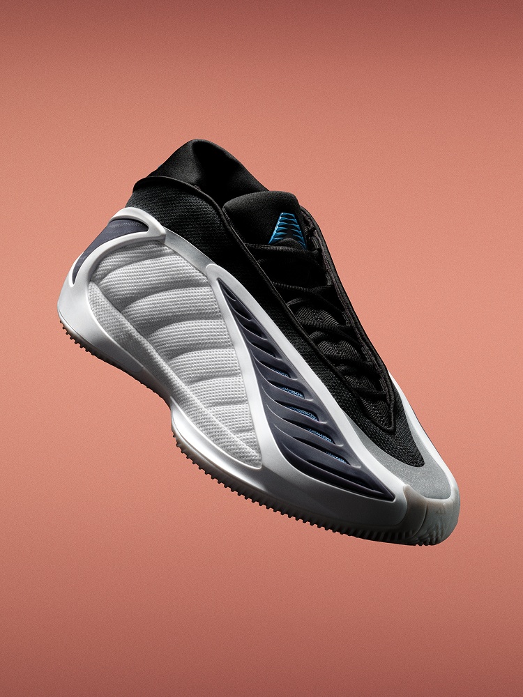 สนีกเกอร์บาสเกตบอลอาดิดาส Anthony Edwards 2 สีดำและขาวจากอาดิดาสถูกจัดวางเป็นมุมตัดกับพื้นหลังสีส้ม มีพื้นรองเท้าแกะสลักและดีไซน์ด้านข้างที่เหมือนคลื่น