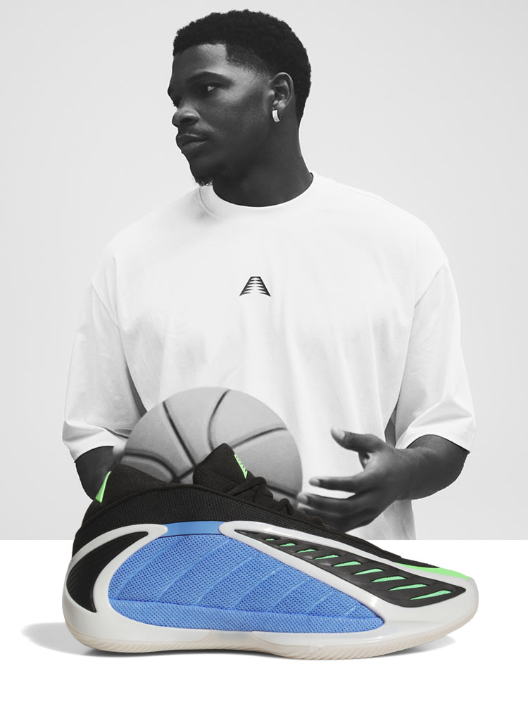 The image depicts a young man wearing a white t-shirt and holding a basketball. The background is plain and neutral, allowing the focus to remain on the subject and the basketball sneakers he is showcasing.