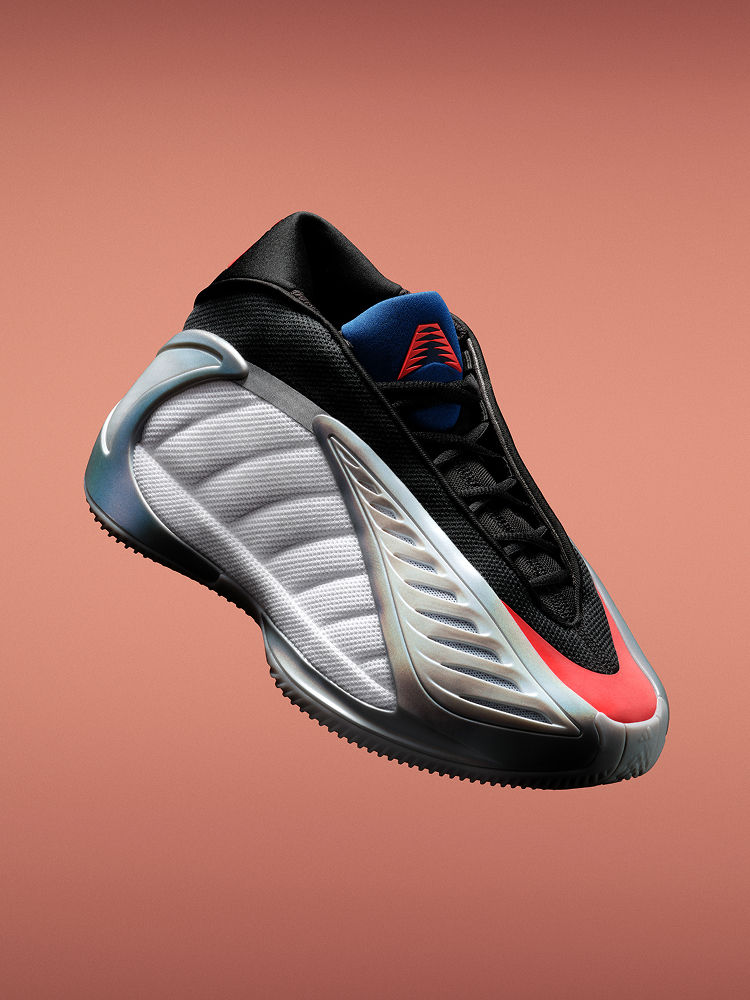 A black, grey and red adidas Anthony Edwards 2 basketball sneaker shown angled against a orange background. It has a sculpted sole and wave-like side design.