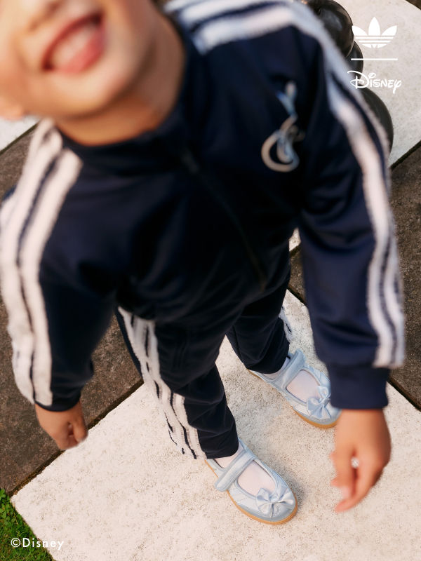 A young child wearing a navy blue tracksuit with white stripes, standing on a concrete surface.