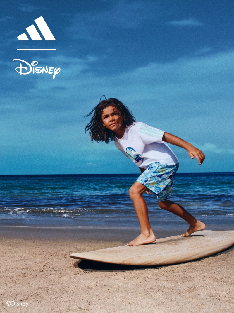 A person in casual clothing is surfing on a beach with a clear blue sky and ocean in the background.