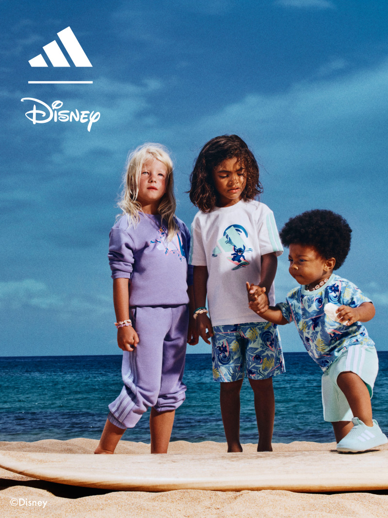 Three children, two girls and one boy, standing on a wooden platform with a blue ocean and sky in the background.