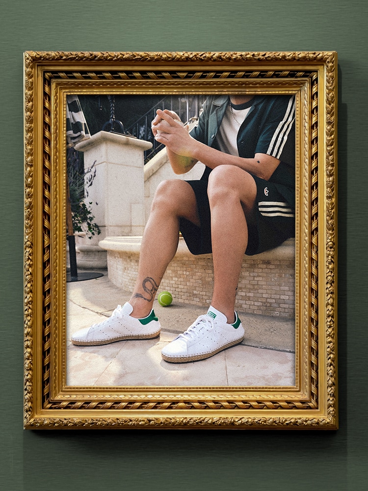 Edison Chen seated wearing the adidas x Edison Chen CLOT Stan Smith Collection, featuring green shorts with the Trefoil logo and three stripes, and a matching camp collar shirt.