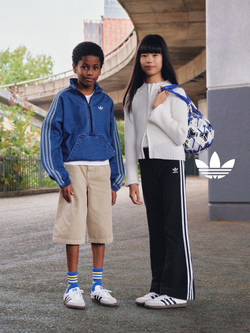 A girl and a boy in adidas apparel and white Samba shoes pose underneath a concrete bridge in daylight.