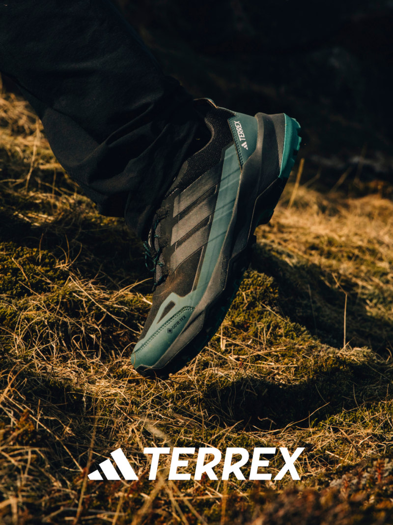 Close-up of a black and blue Skychaser AX5 GTX shoe worn while hiking uphill in grassy terrain.