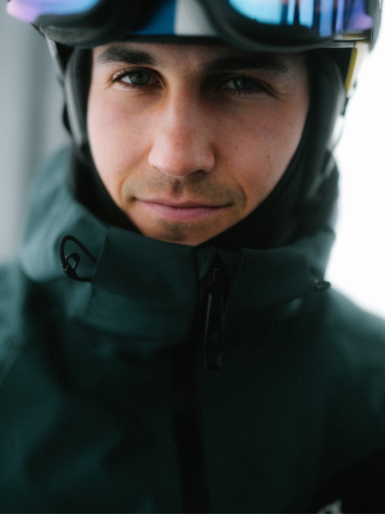 Eine Person, die eine grüne Jacke und einen grünen Helm mit einer ernsten Miene im Gesicht trägt, scheint sich im Freien zu befinden.