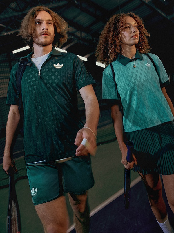 A male and female tennis player wearing matching green adidas tennis outfits, standing together on a tennis court.