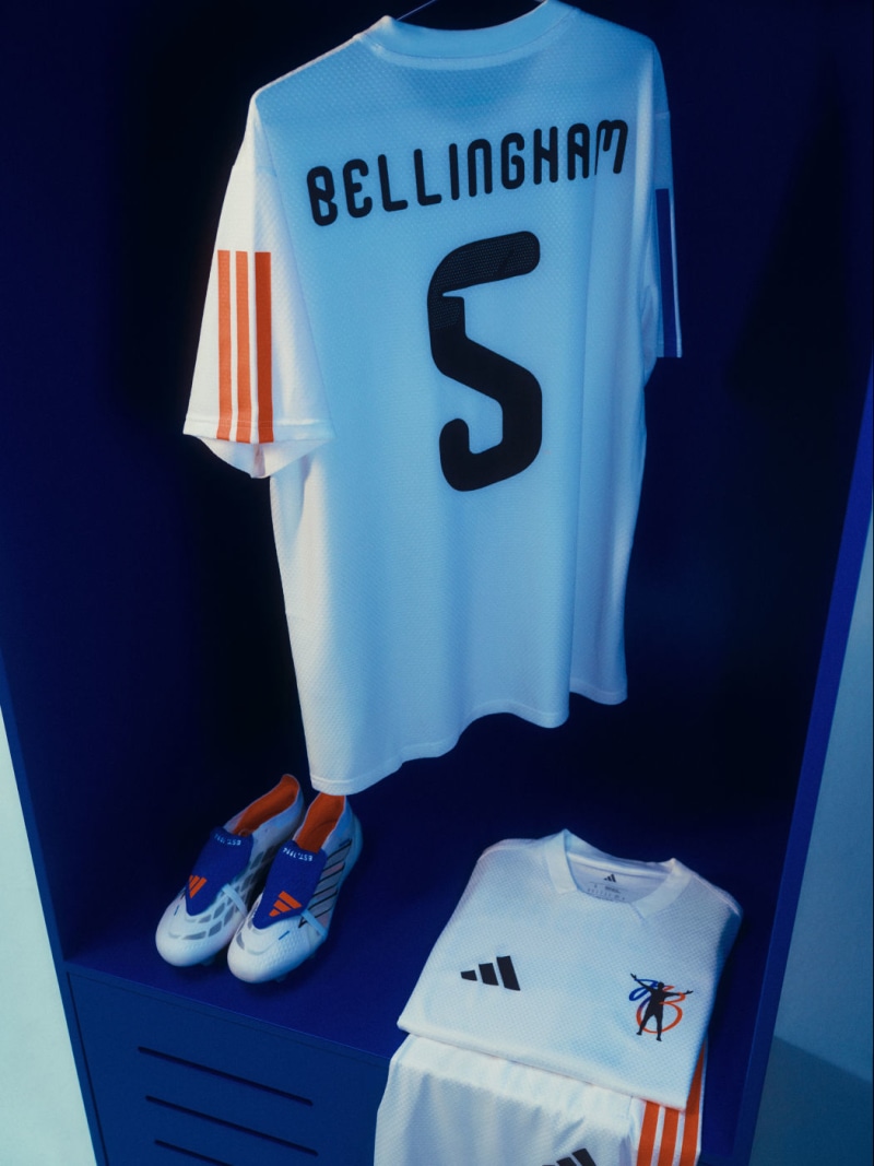 Denne Jude Bellingham-trøje fra adidas hænger i et skab med røde, hvide og blå Predator-støvler, der er pænt placeret nedenunder.