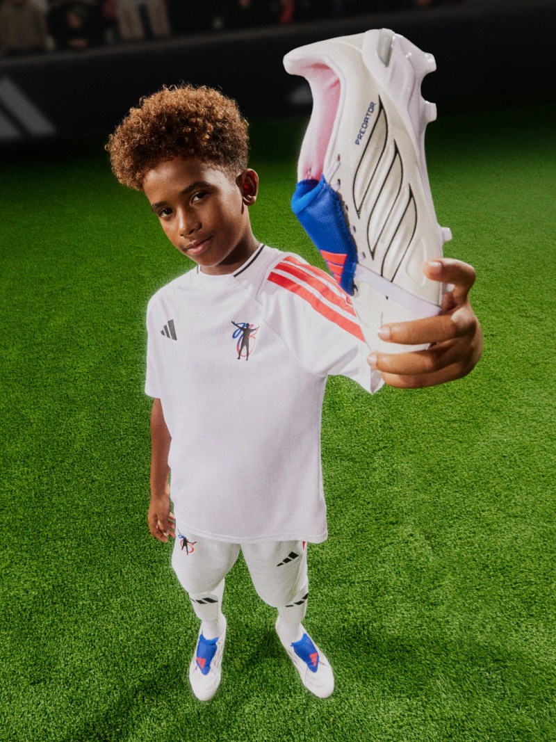 A young boy with curly brown hair poses playfully while showing off the adidas Jude Bellingham kids collection.
