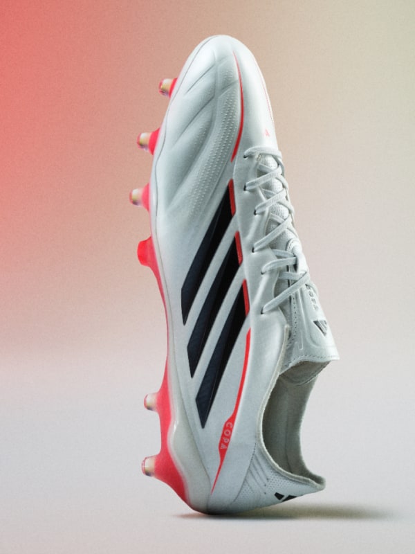 A white and black soccer cleat with red accents, set against a plain pink background.