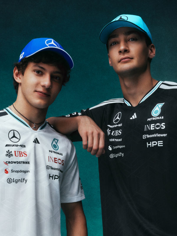 Two young men wearing matching blue and white uniforms with various sponsor logos, standing together in front of a dark green background.