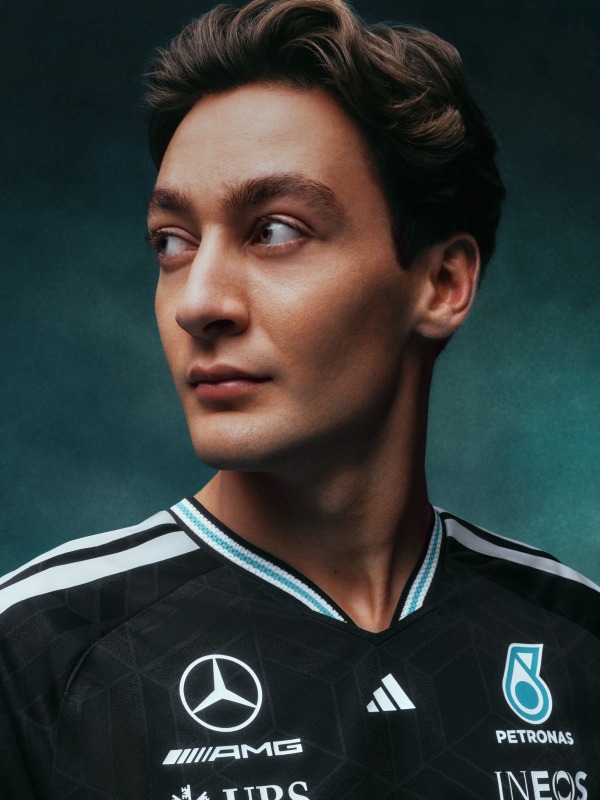 A young man with dark hair and a serious expression, wearing a black sports jersey with white and blue accents, stands against a dark green background.