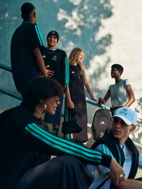 A group of people, some wearing Adidas sportswear, standing in front of a building with a blue sky and trees in the background.