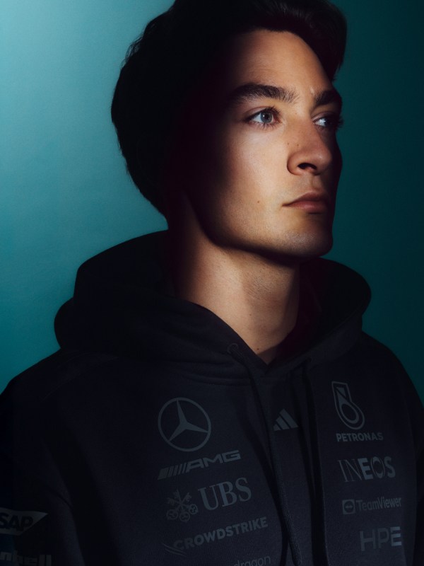 A young man with a serious expression, wearing a black hooded sweatshirt, set against a teal-coloured background.
