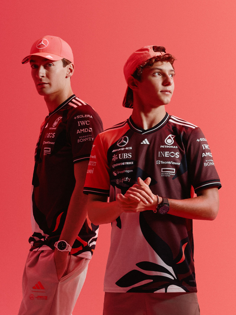 Two individuals wearing red sports jerseys and caps stand together against a vibrant red background.