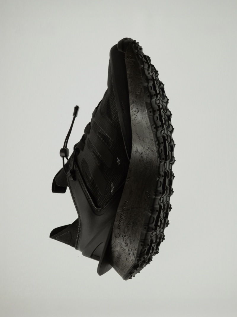 Ett svart, texturerat objekt med en grov, oregelbunden yta verkar vara i fokus för bilden, placerat mot en enkel, ljusfärgad bakgrund.