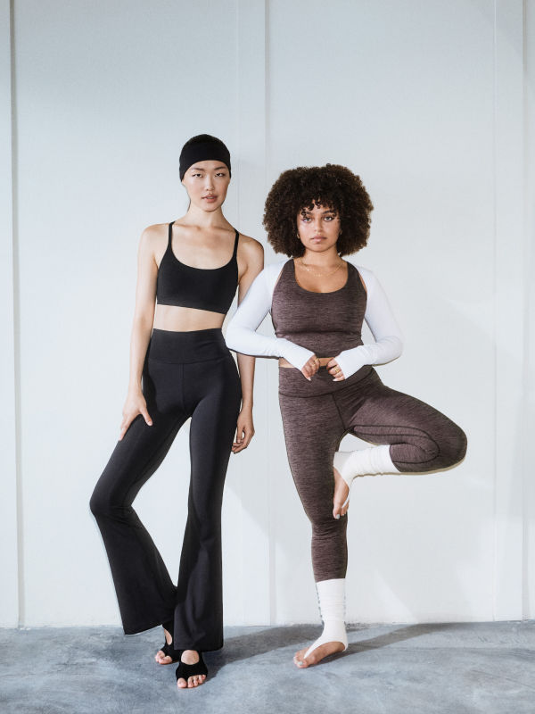 Two women in athletic wear, one with straight black hair and the other with curly dark hair, are posing against a plain white background.