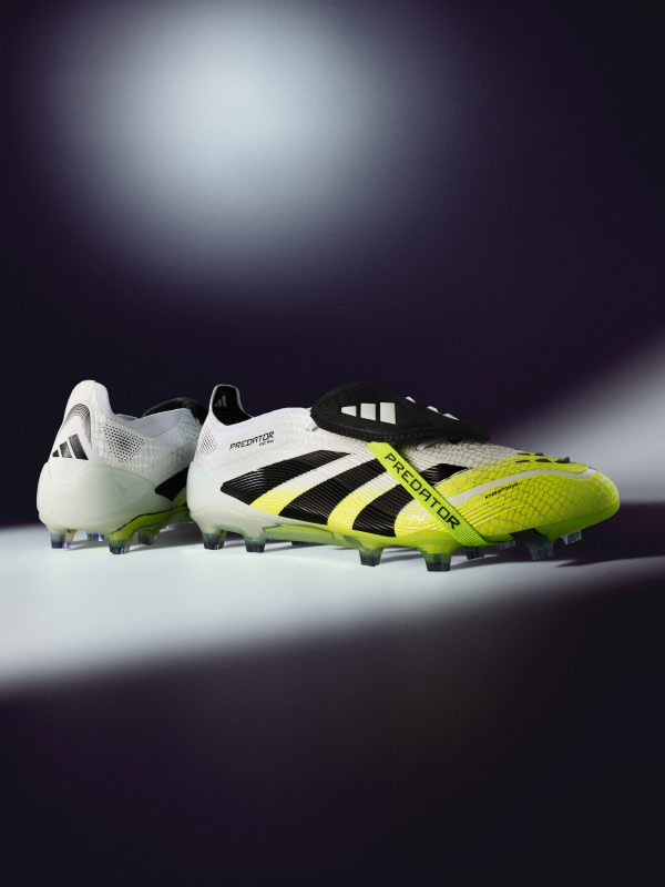 A pair of white and neon yellow soccer cleats are prominently displayed against a dark, shadowy background, creating a dramatic and striking visual composition.