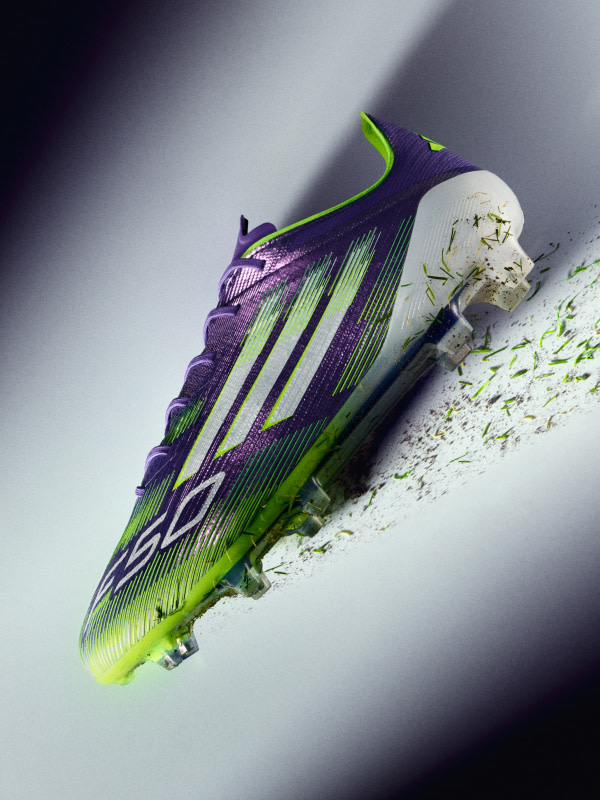 A vibrant purple and green soccer cleat with a white sole rests on a dark background, creating a striking visual contrast.