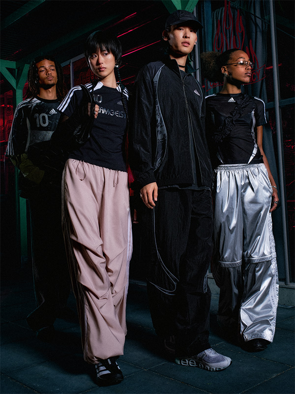 스타일리시한 블랙과 핑크 아웃핏을 입은 일행은 빨간색과 초록색 조명을 배경으로 희미한 조명 아래 서 있다.