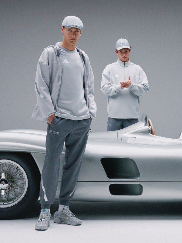Two individuals wearing matching gray athletic attire stand in front of a sleek, silver sports car.
