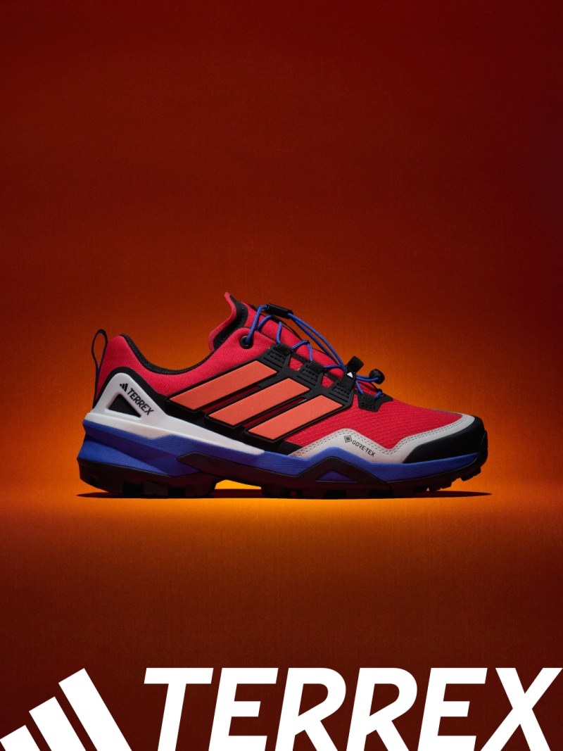 A vibrant red and black Adidas Terrex outdoor shoe stands prominently against a fiery orange background.