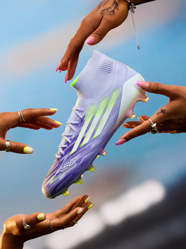Hands reaching out to catch a purple and white F50 Sparkfusion soccer boot  against a bright blue sky.