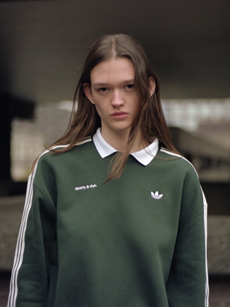 A young person with long dark hair wearing a green sports jersey stands in front of a blurred background.