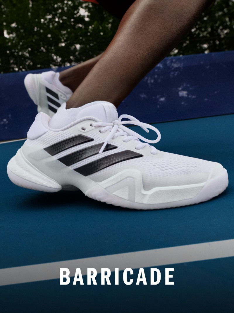 The image shows a pair of white and black athletic shoes resting on a blue surface, with the word "BARRICADE" prominently displayed in the foreground.