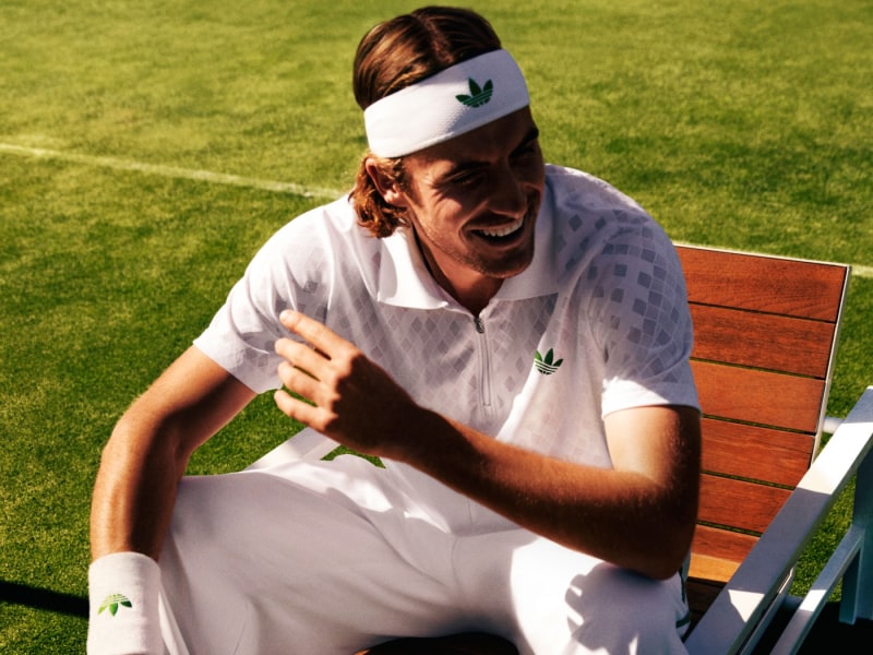 A person wearing a white shirt and headband with a leaf logo is sitting on a wooden bench on a grassy field.
