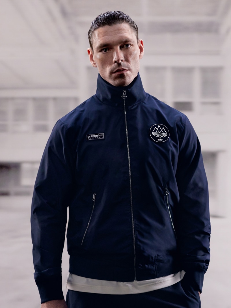 A photograph depicts British actor James Nelson-Joyce in an adidas SPZL track jacket.