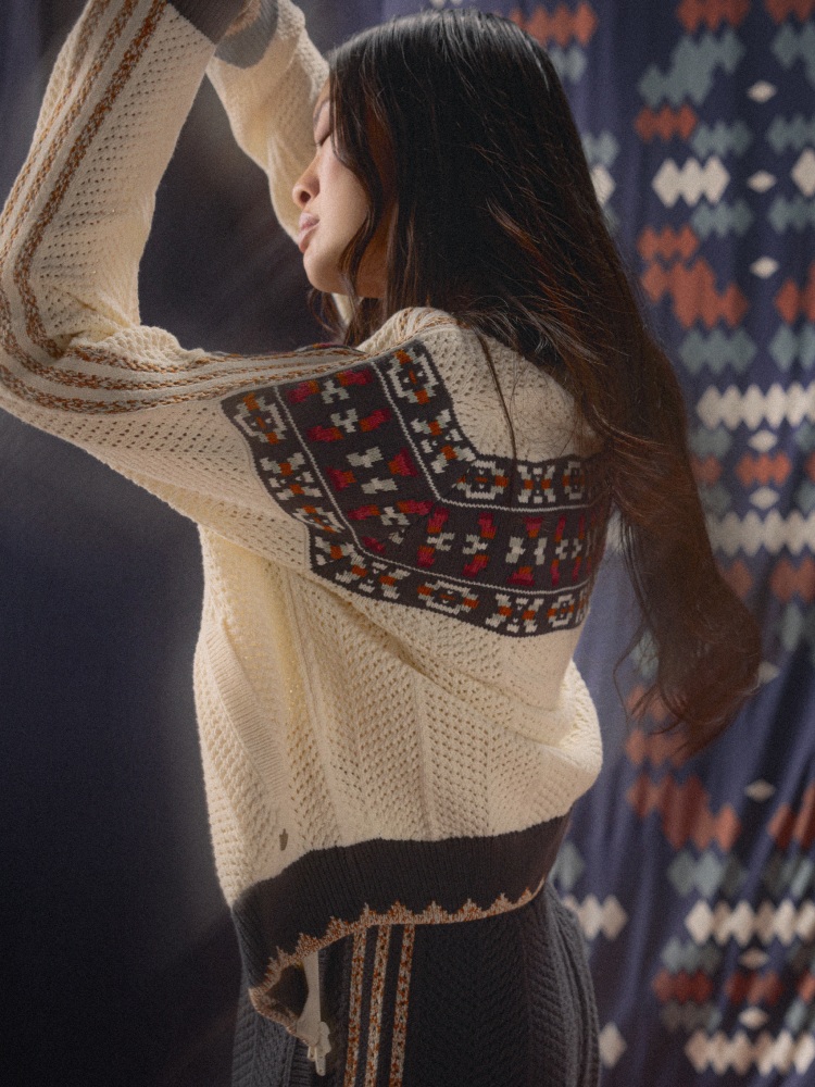 A woman dances in a cream crochet knitted adidas jacket with a geometric pattern and three beige adidas stripes along the sleeve.