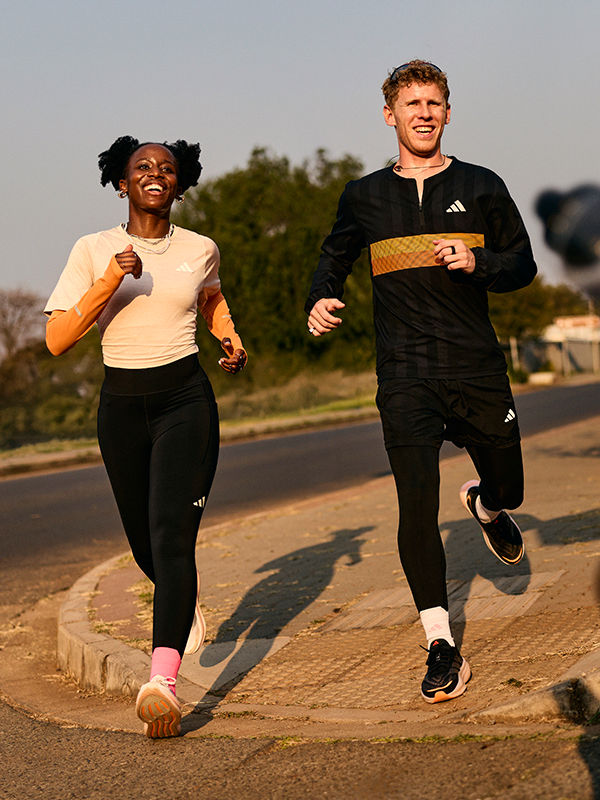 Two people, a woman and a man, are jogging together on a dirt path surrounded by trees and a clear sky in the background.