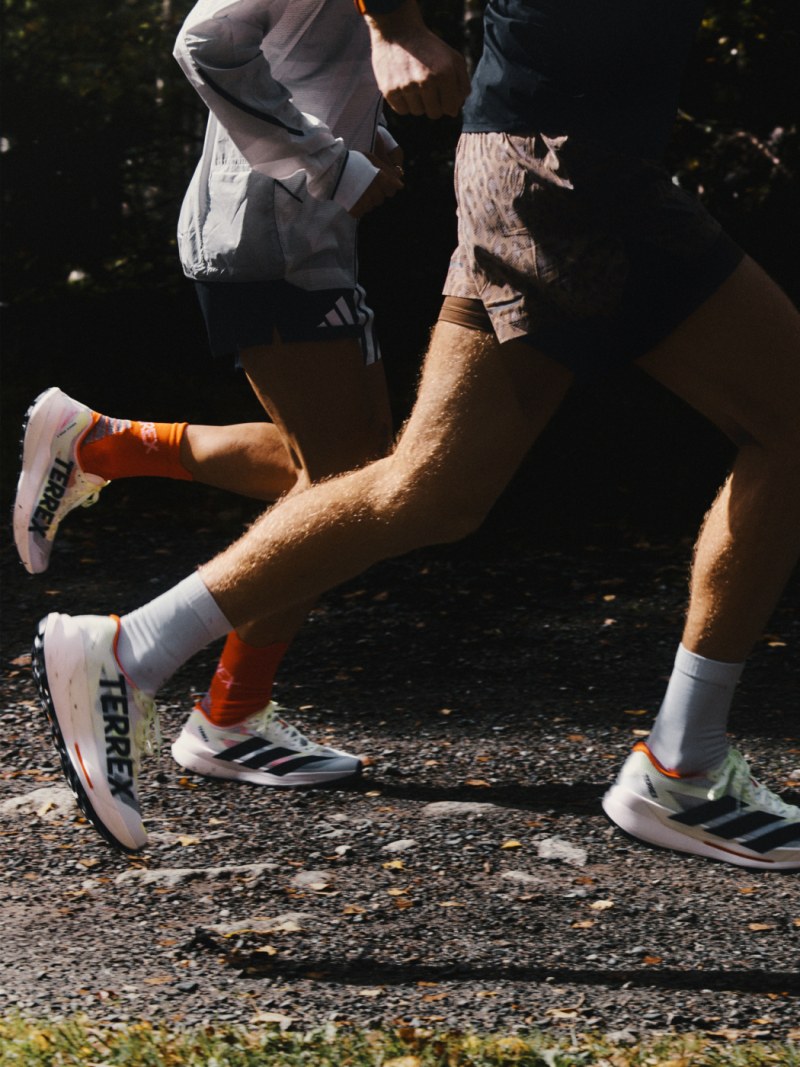 The image shows the lower body and legs of two people engaged in a running activity on a gravel path, with the background appearing to be a dimly lit outdoor setting.