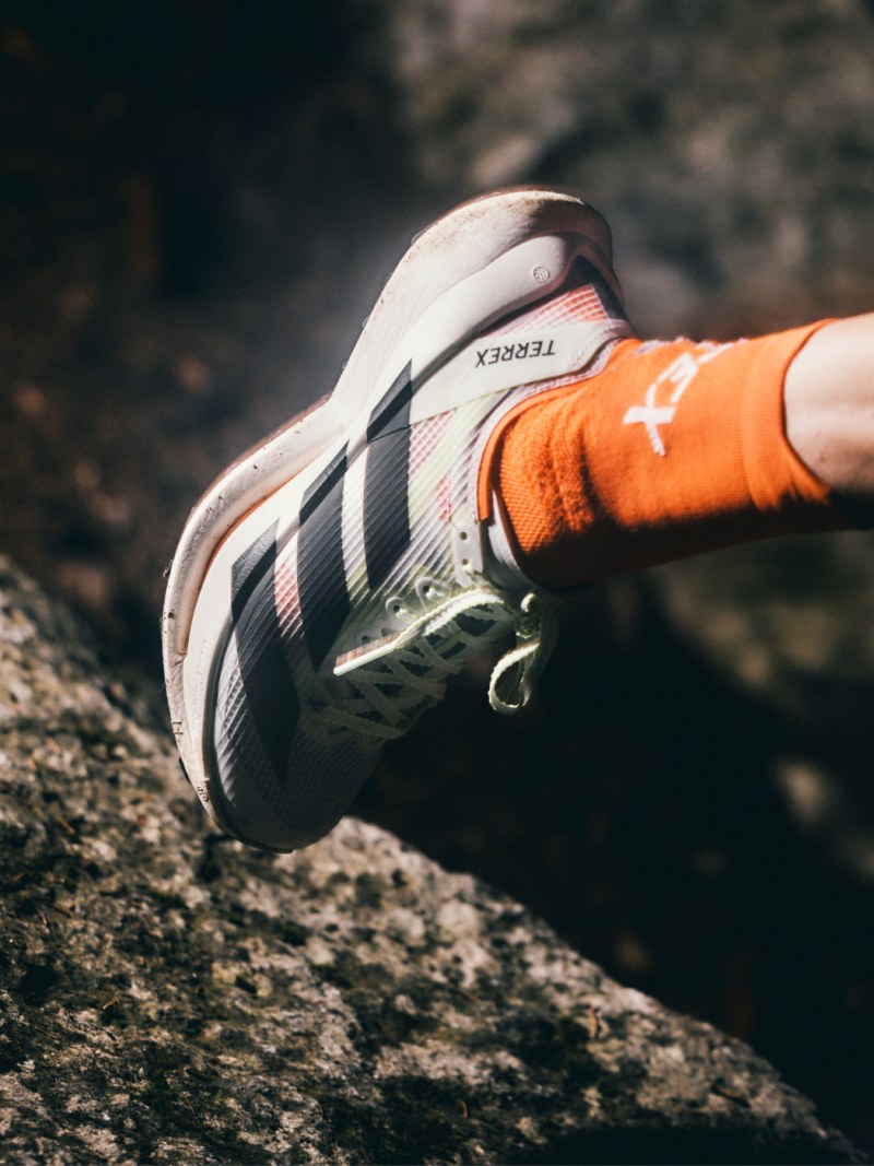 A close-up view of a person's foot wearing a white and orange athletic shoe on a rocky surface.