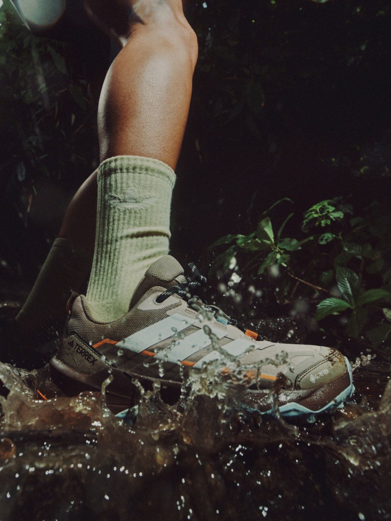 บนร่างกายและเท้าของแต่ละคนสามารถมองเห็นได้ โดยสวมรองเท้าเดินป่าที่สวมใส่และมีโคลน ยืนอยู่ในแอ่งน้ำที่ล้อมรอบไปด้วยต้นไม้เขียวชอุ่ม