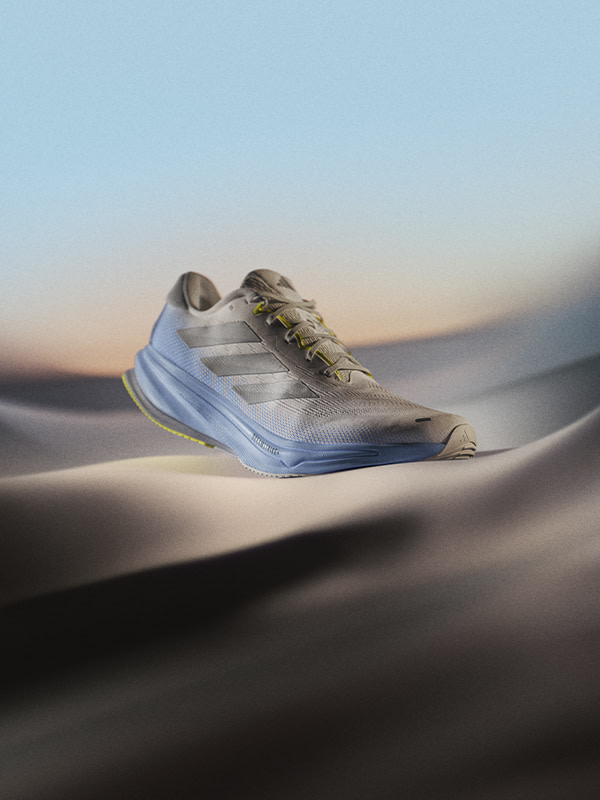 A pair of gray and white athletic shoes rests on a sandy desert landscape, with a hazy, colorful sky in the background.