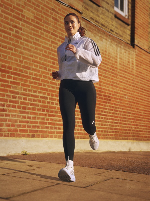 A young woman in athletic clothing is jogging on a brick-paved surface in front of a brick building.