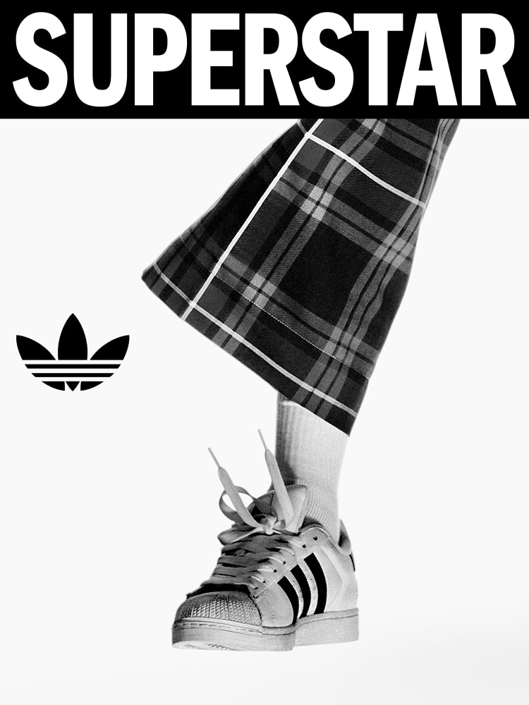 Close-up of a foot in adidas Superstar shoes with white socks and plaid pants.