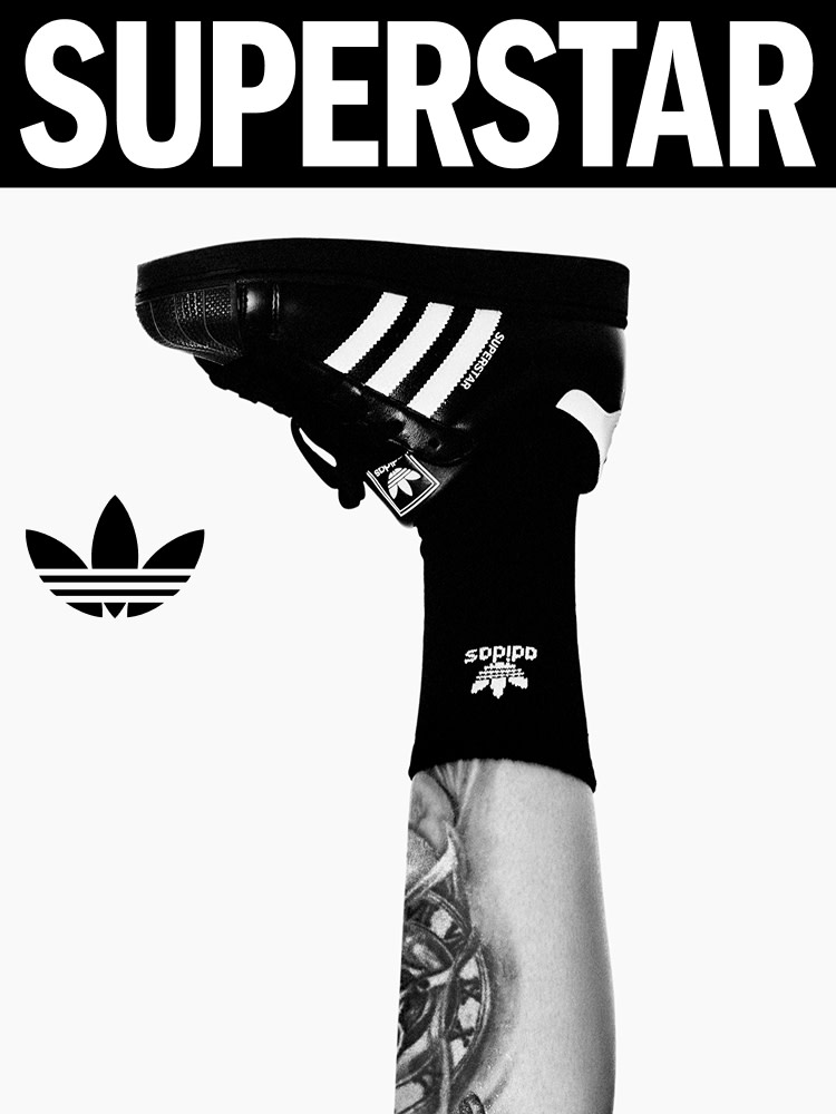 Tattooed leg raised vertically, wearing black adidas socks and black adidas Superstar shoe.