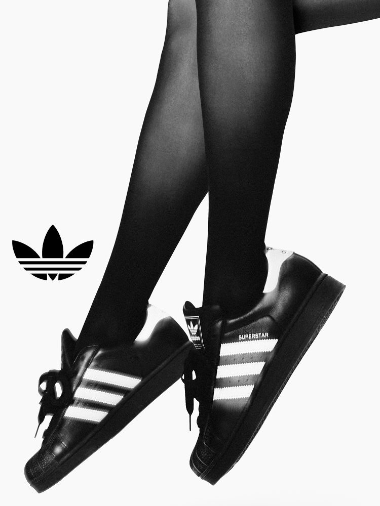 Close-up of legs in black tights wearing black adidas Superstar shoes with white stripes.